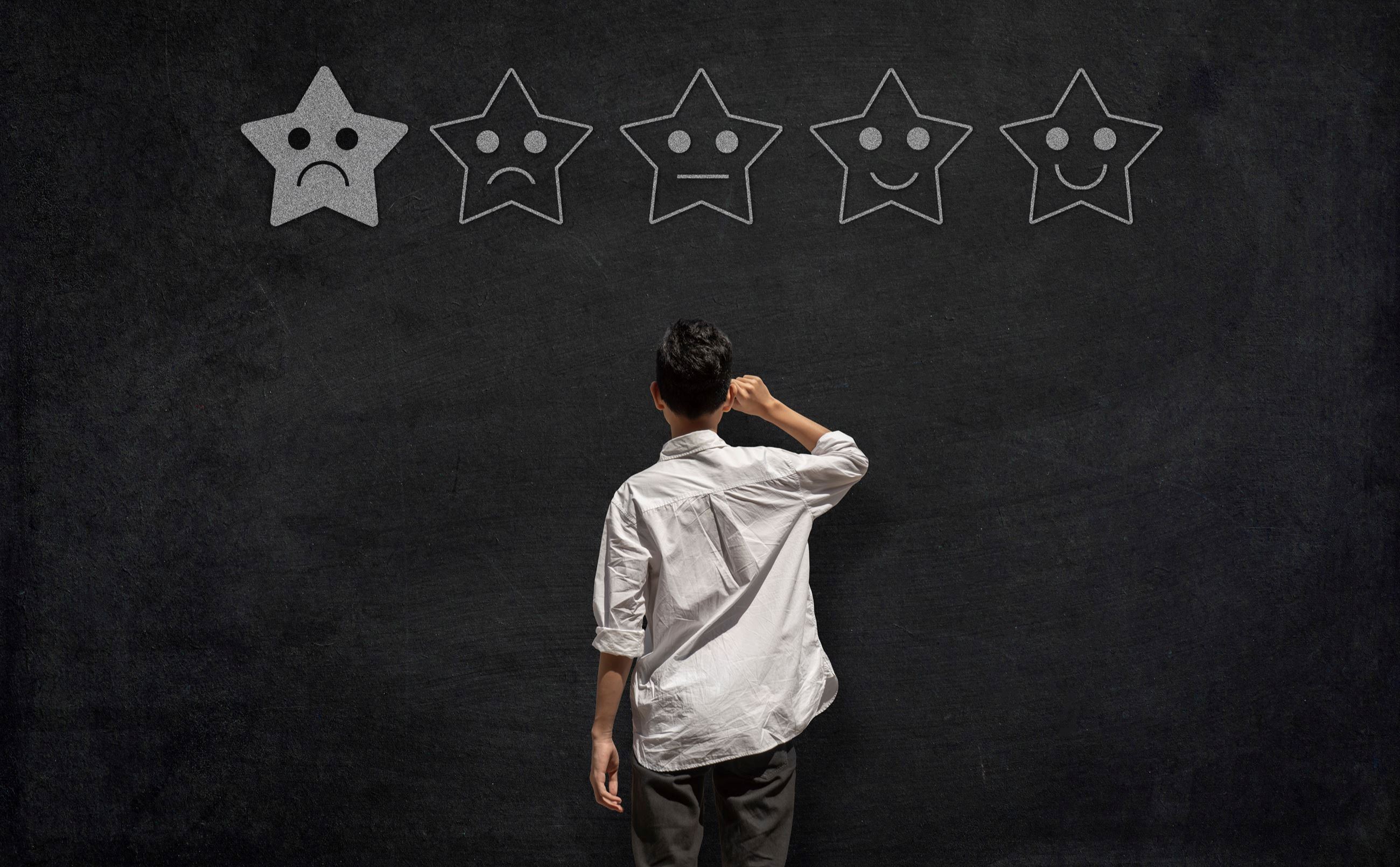 Person facing a black wall that has five stars, with only one filled in.